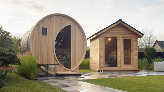 A cedar barrel sauna and a cedar cabin sauna standing side by side on a landscaped garden patio
