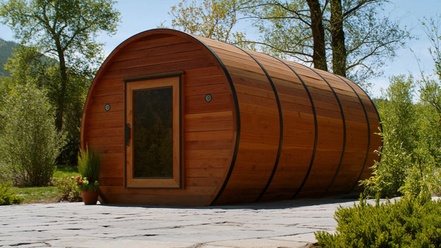 Western red cedar barrel sauna with black steel band hoops on a stone patio in a mountain garden