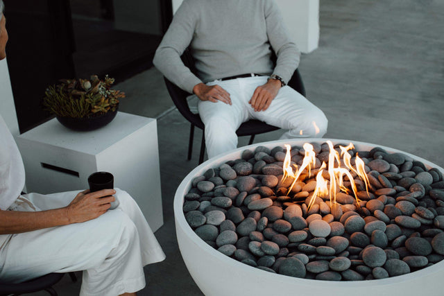 HPC Dekko Serenade 40 concrete fire table in Natural with Slate Beachstone media, lit beside seated guests