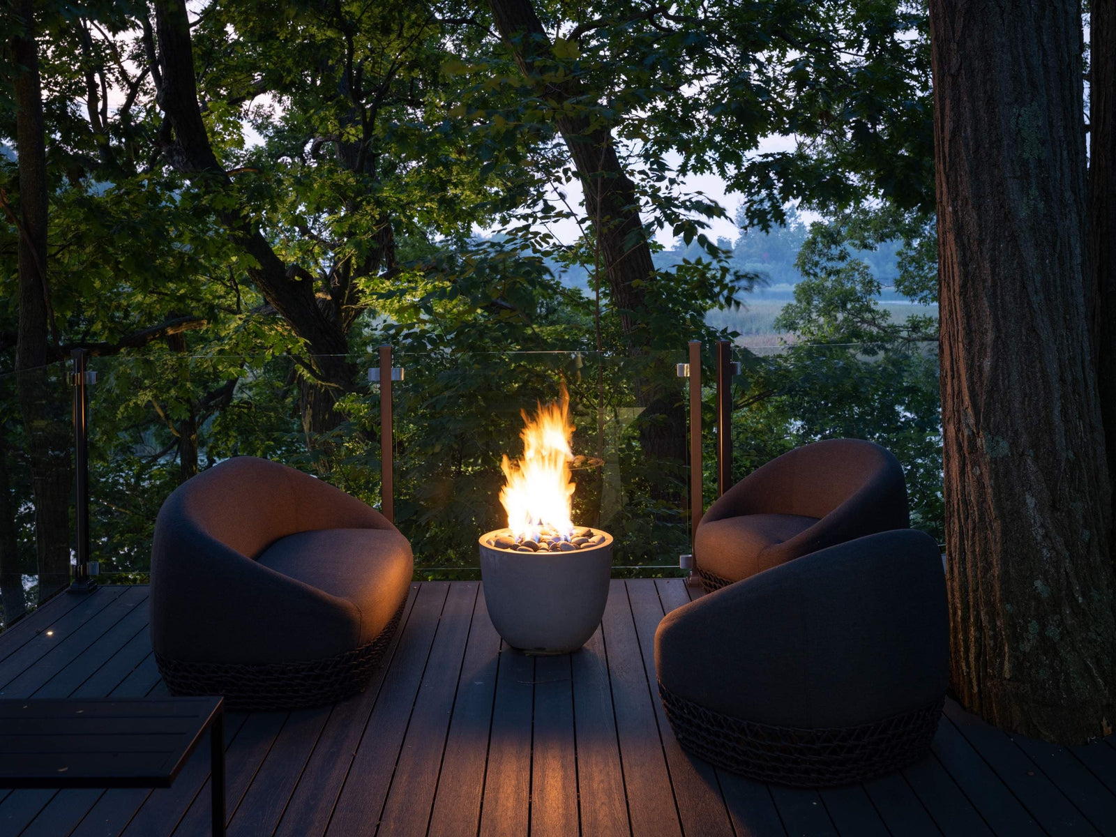 HPC Dekko Element concrete fire table in Ash with Ivory Beachstone media, lit at dusk on a timber deck