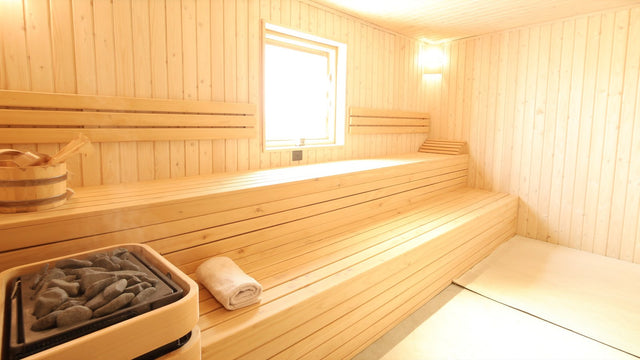 Interior of a traditional Finnish sauna with cedar benches, an electric stove filled with sauna rocks, and a wooden bucket and ladle