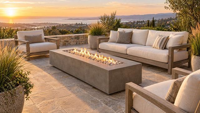 Long rectangular concrete gas fire table surrounded by lounge seating on a stone patio at sunset (illustration)
