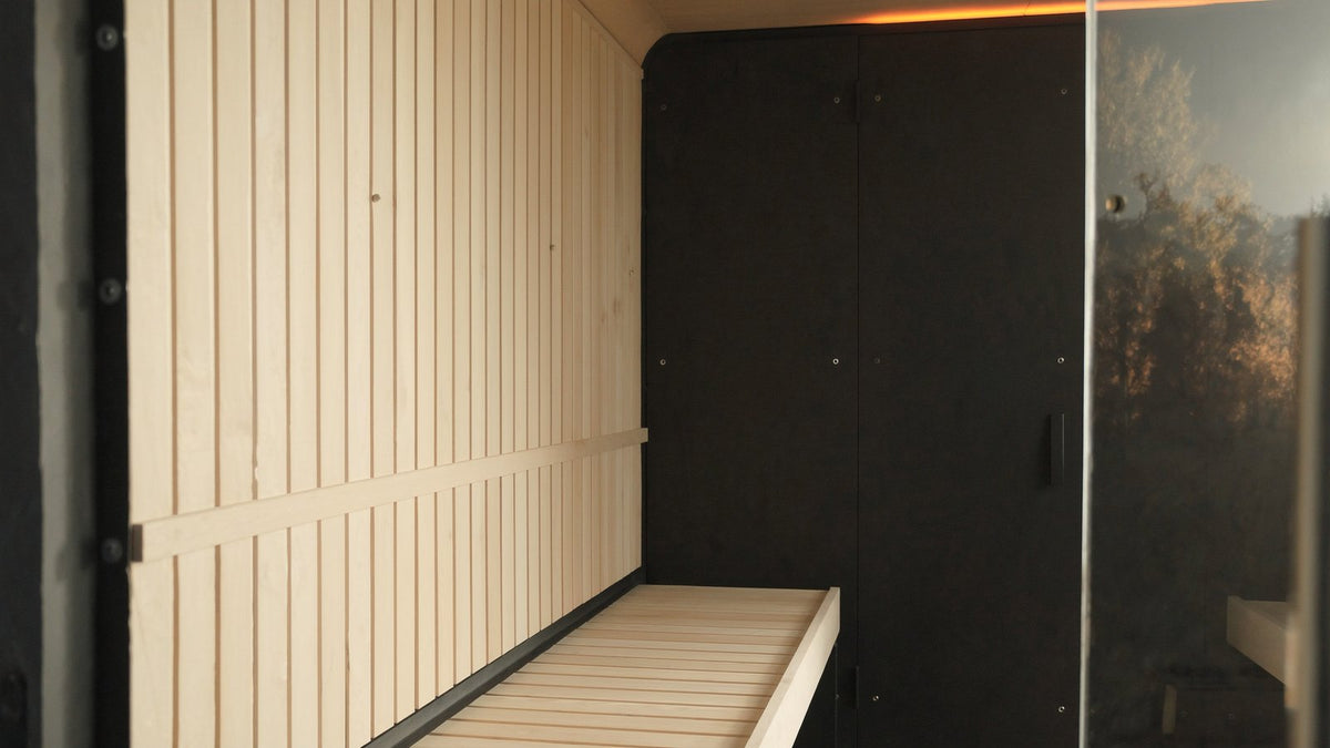 Interior of a modern infrared sauna cabin with pale hemlock walls, a bench and flat black carbon heating panels