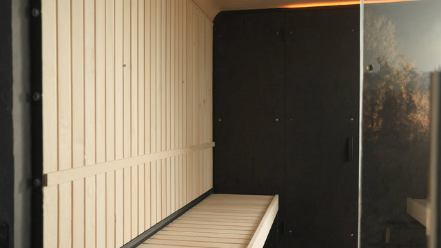Interior of a modern infrared sauna cabin with pale hemlock walls, a bench and flat black carbon heating panels