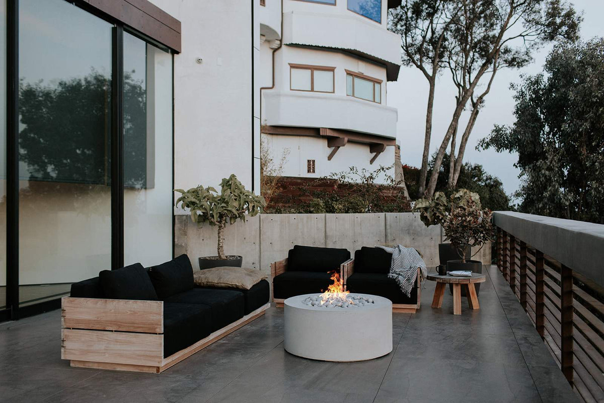 A round Dekko concrete fire pit burning on a terrace between two low sofas at dusk